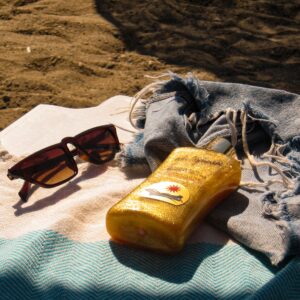 Sunglasses and sunscreen on a towel by the beach, capturing the essence of summer relaxation.